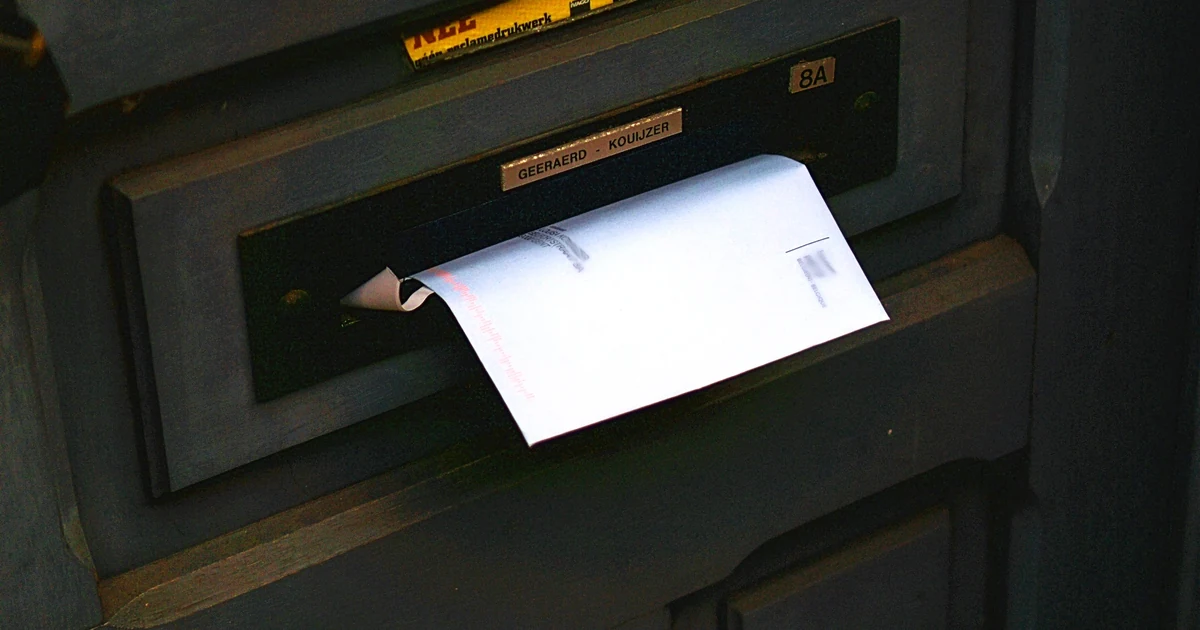 A white envelope pushed halfway through the mail slot of a dark front door.